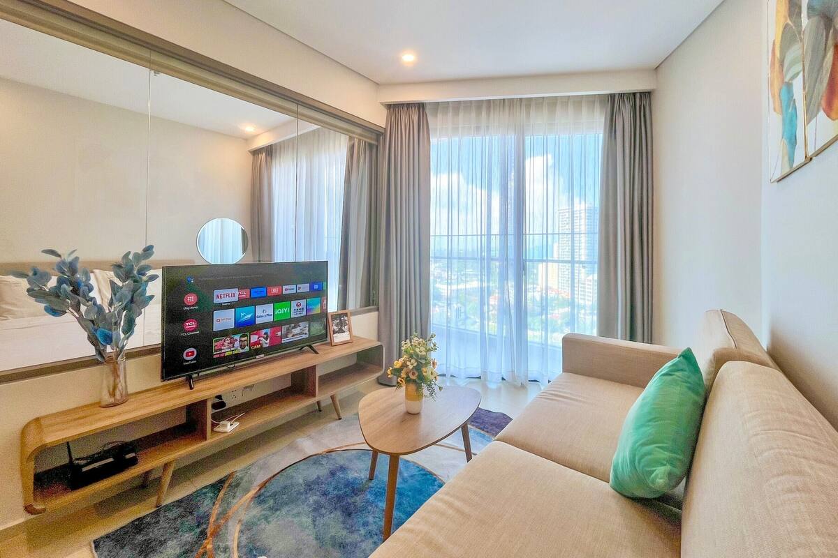 Una habitación de hotel moderna con una gran televisión de pantalla plana, un sofá, una mesa de centro y vistas de la ciudad a través de amplios ventanales.