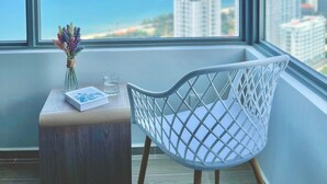 A room with a large window, a white chair, a small wooden table, and a vase with flowers. - The Song Sunny Canopy (Ho Chi Minh City)