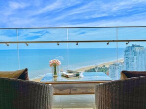 A balcony with wicker furniture, a glass table, and a vase of flowers.