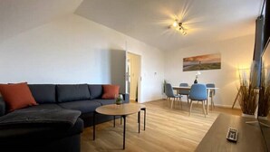 A modern living room with a dark-colored sofa, a round coffee table, and a dining area with a table and chairs.