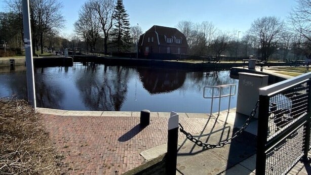 A canal with a house in the background, a bridge, and a clear sky.