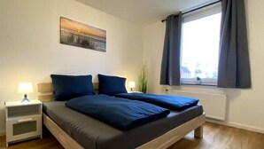 A bedroom with a bed, bedside tables, a window with curtains, and a wall-mounted painting.