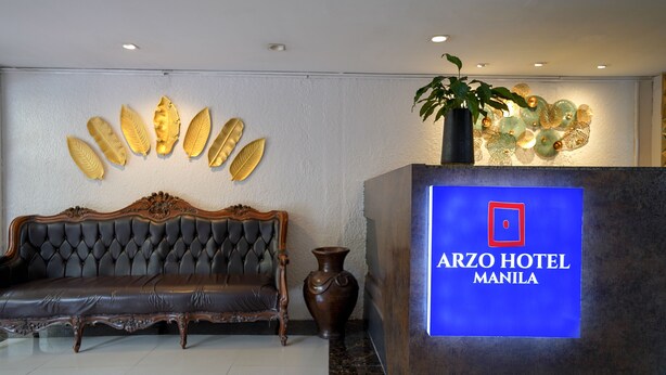 A reception area with a dark leather sofa, a decorative wall with golden leaf patterns, and a reception desk displaying the Arzo Hotel Manila logo. - Arzo Hotel Manila (Manila)