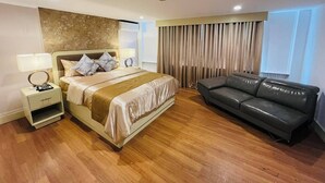 A hotel room with a bed, a nightstand, a lamp, a sofa, and a large window with curtains. - Arzo Hotel Manila (Manila)