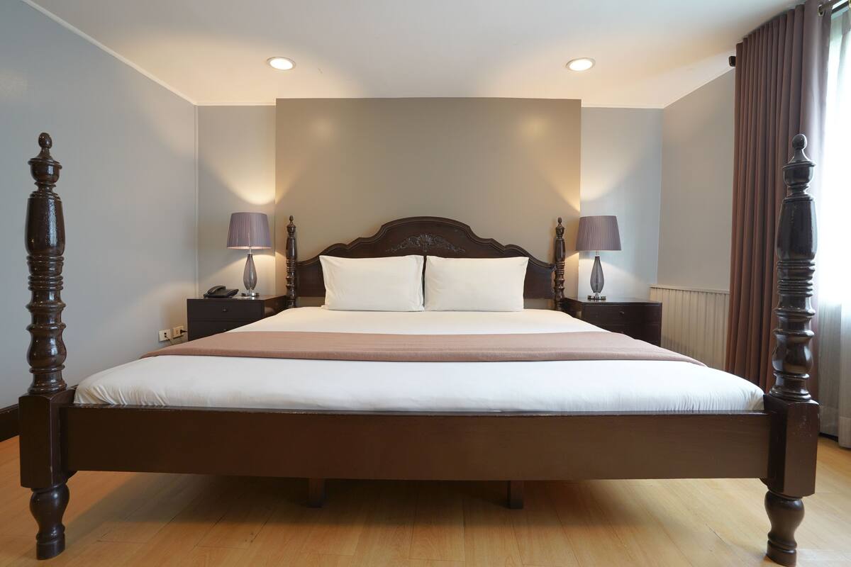 A large bed with a wooden frame, two bedside tables with lamps, and a headboard with a light fixture.
