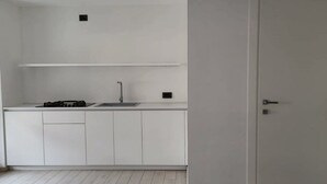 A small, white kitchen with a single sink, a stove, and cabinets. There is a door on the right side of the image.