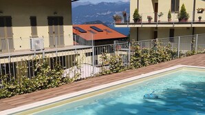 A swimming pool with a view of mountains in the background, surrounded by buildings with balconies and potted plants.