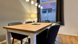 Un coin repas avec une table en bois, quatre chaises, une lampe et une vue sur un bâtiment en briques, visible à travers une fenêtre.