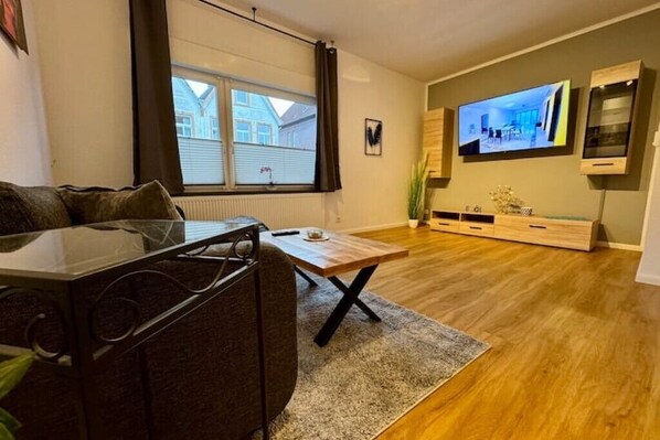 Una sala de estar moderna con un sofá, una mesa de centro, un televisor montado en la pared y una ventana con cortinas.