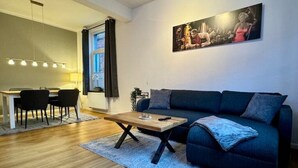 Un salon moderne avec un canapé bleu foncé, une table basse en bois et un coin repas comprenant une table et des chaises.