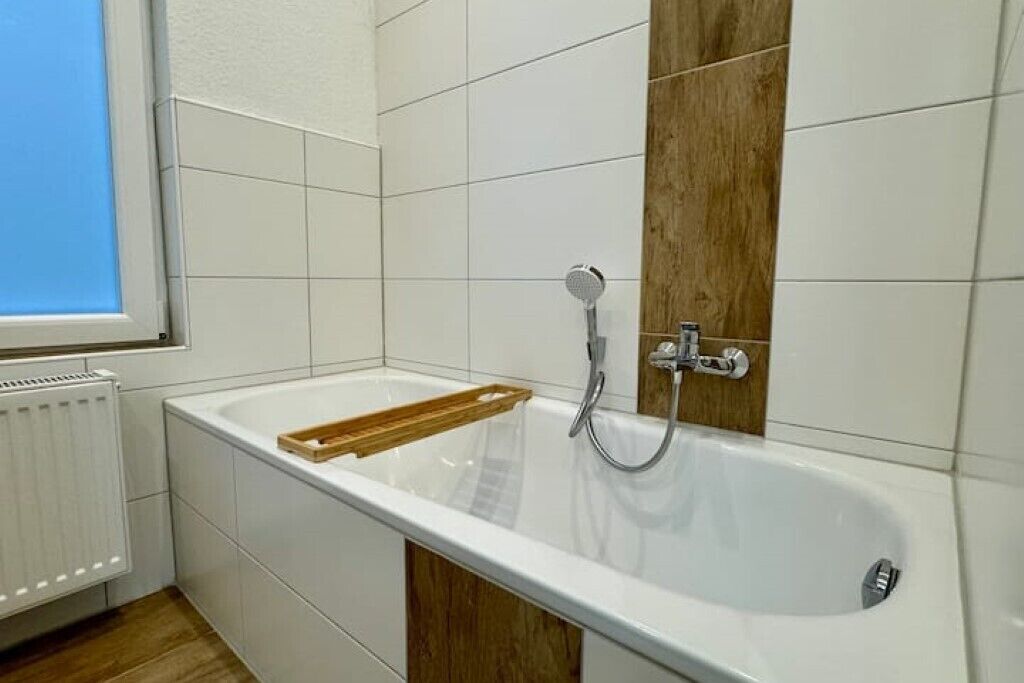 A bathroom with a white bathtub, wooden panel, and white tiled walls.