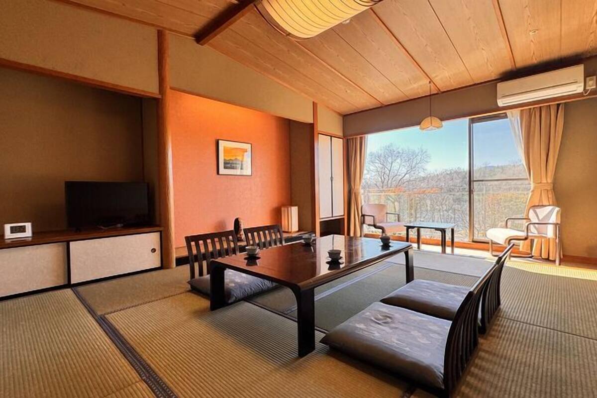 A traditional Japanese-style room with tatami flooring, a low table, and a television on a shelf.