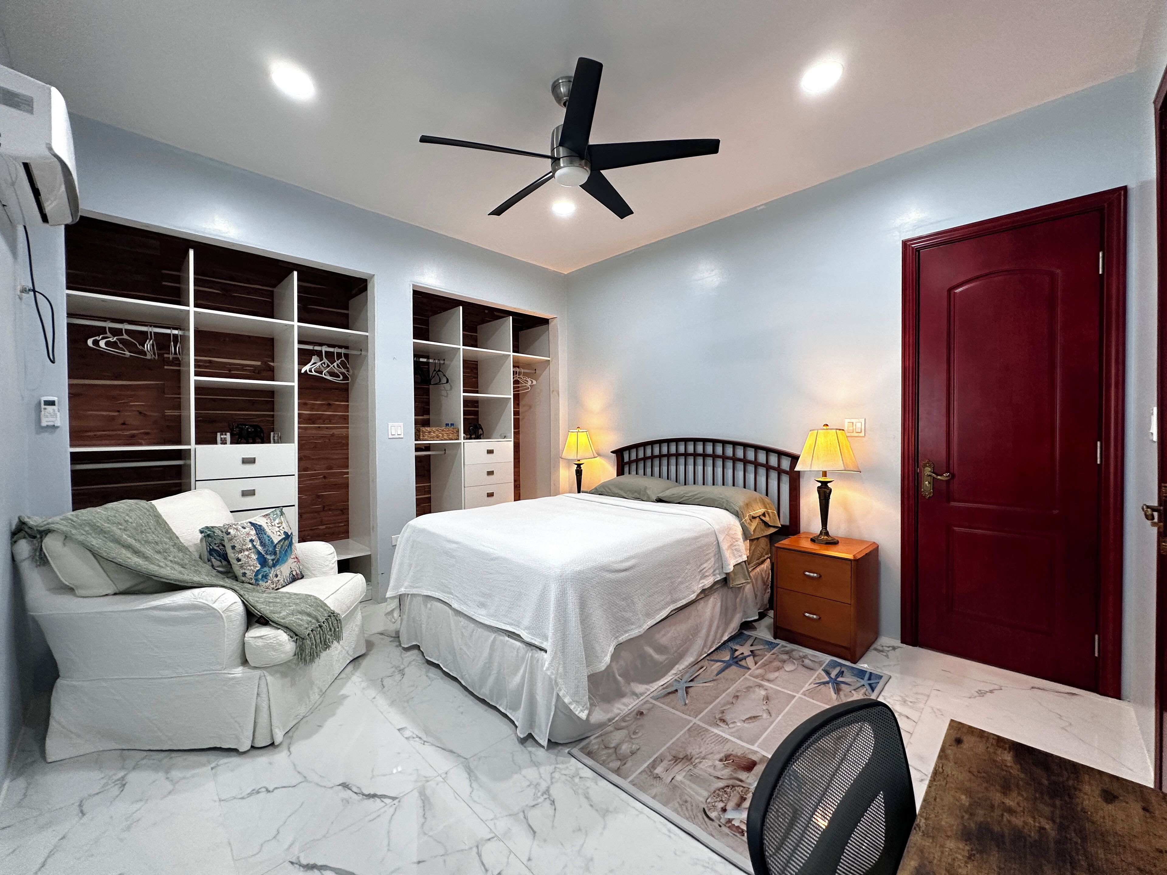 Une chambre à coucher comprenant un lit, des tables de chevet, une armoire et un ventilateur de plafond.