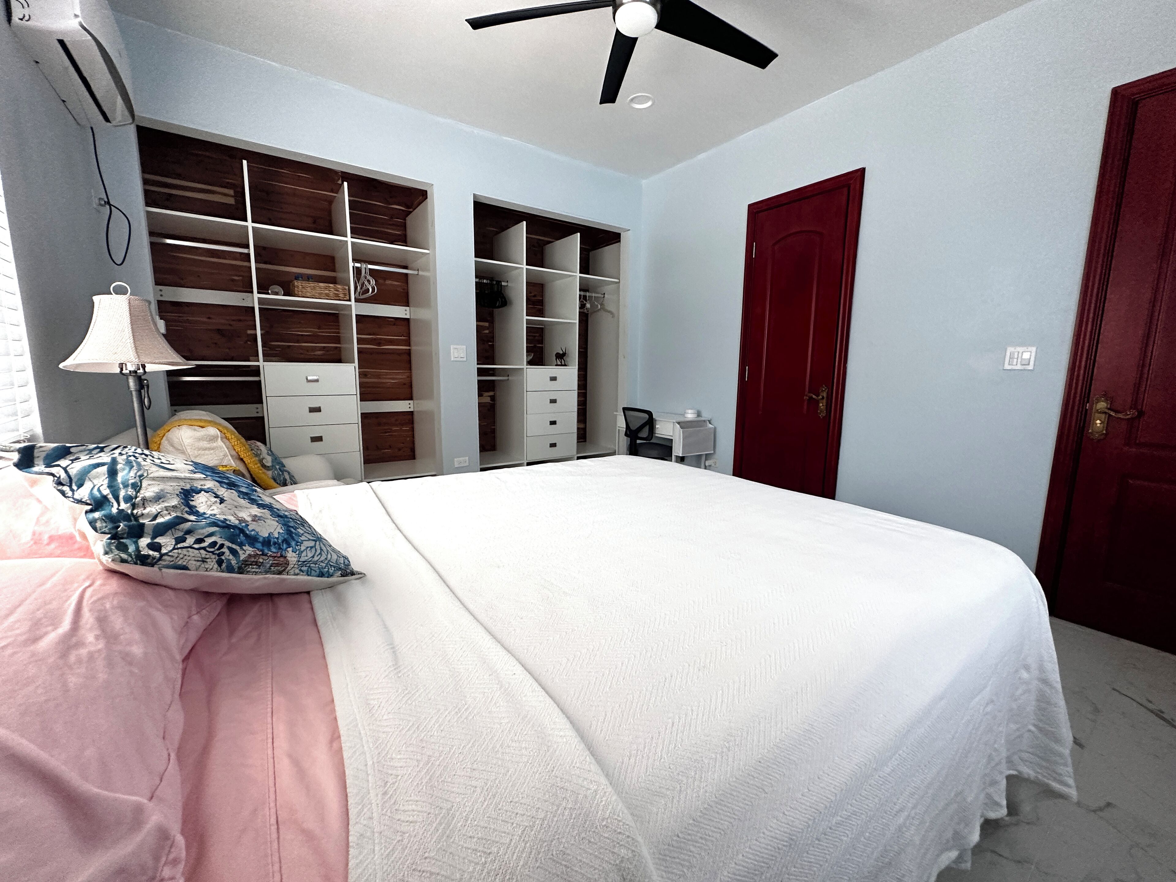 A bedroom with a bed, a desk, a wardrobe, and a red door.