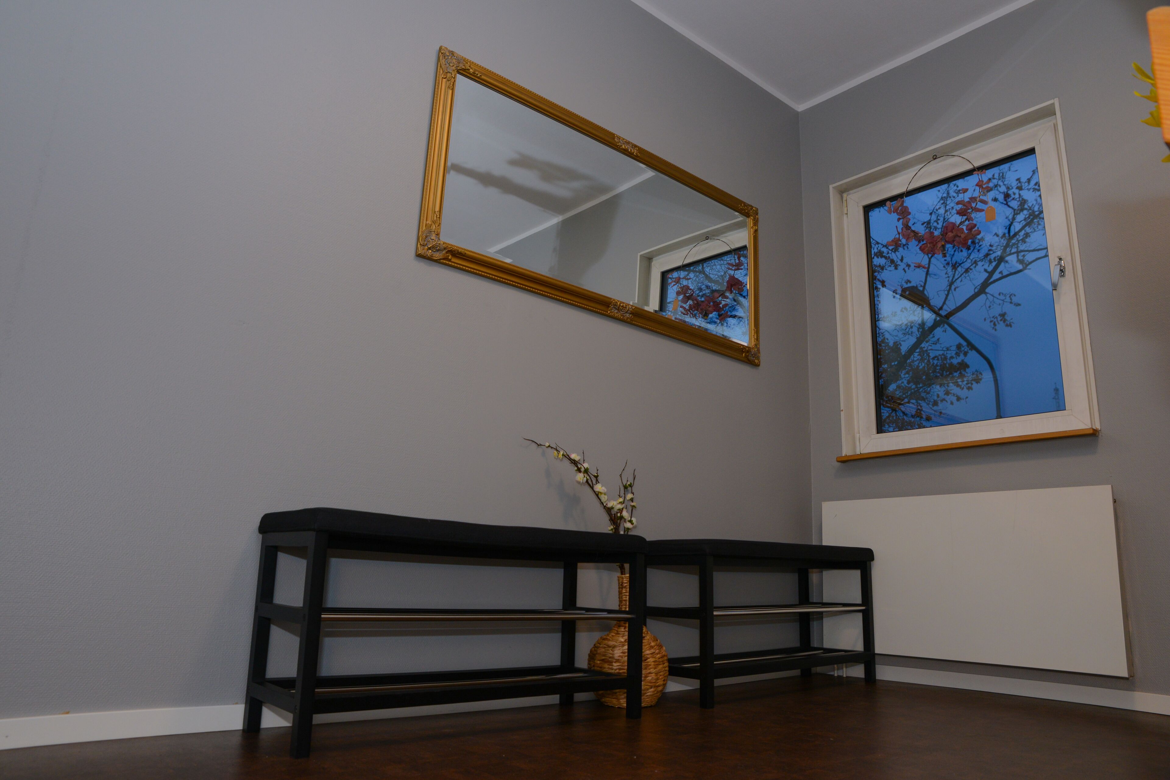 Una habitación con un banco de madera oscura, un espejo grande y una ventana que da a vistas de árboles.