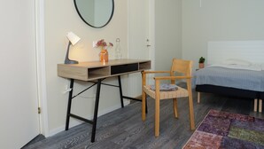 A bedroom with a bed, a desk with a chair, a mirror, and a small potted plant. - Britz Hostel (Kristinehamn)