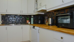 A kitchen with white cabinets, a wooden countertop, a black microwave, and a coffee maker. - Britz Hostel (Kristinehamn)