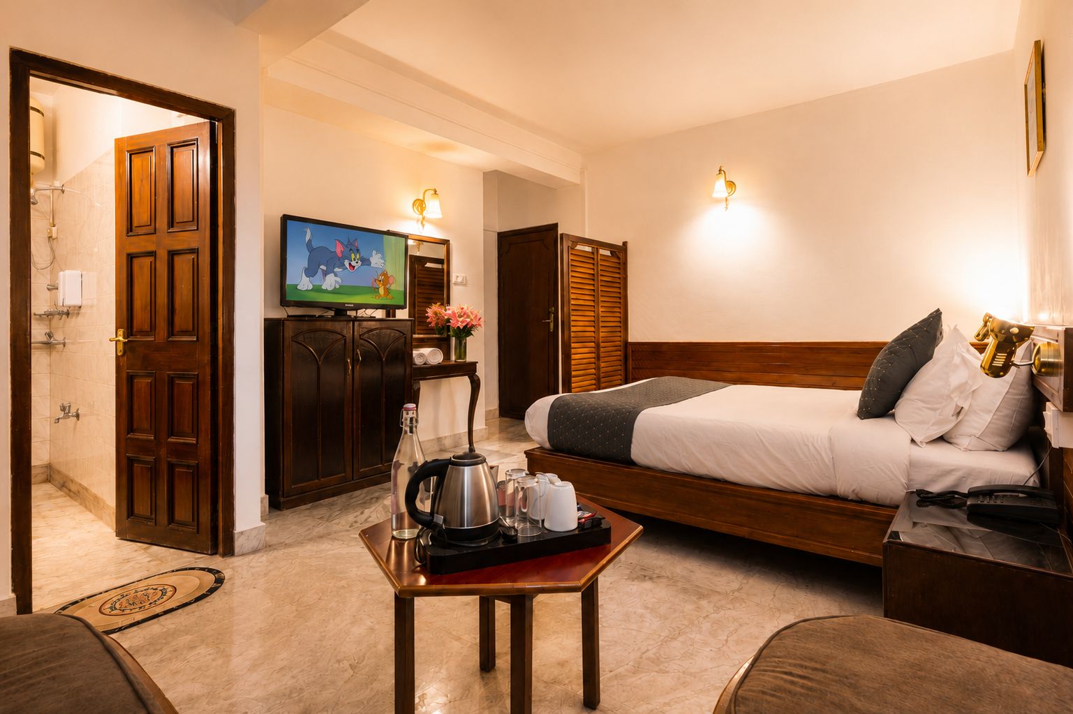 A hotel room with a bed, a television, a coffee table with a kettle, and a wooden wardrobe.