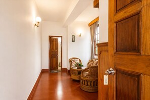 Un couloir avec une porte en bois, des meubles en osier et des luminaires fixés au mur.