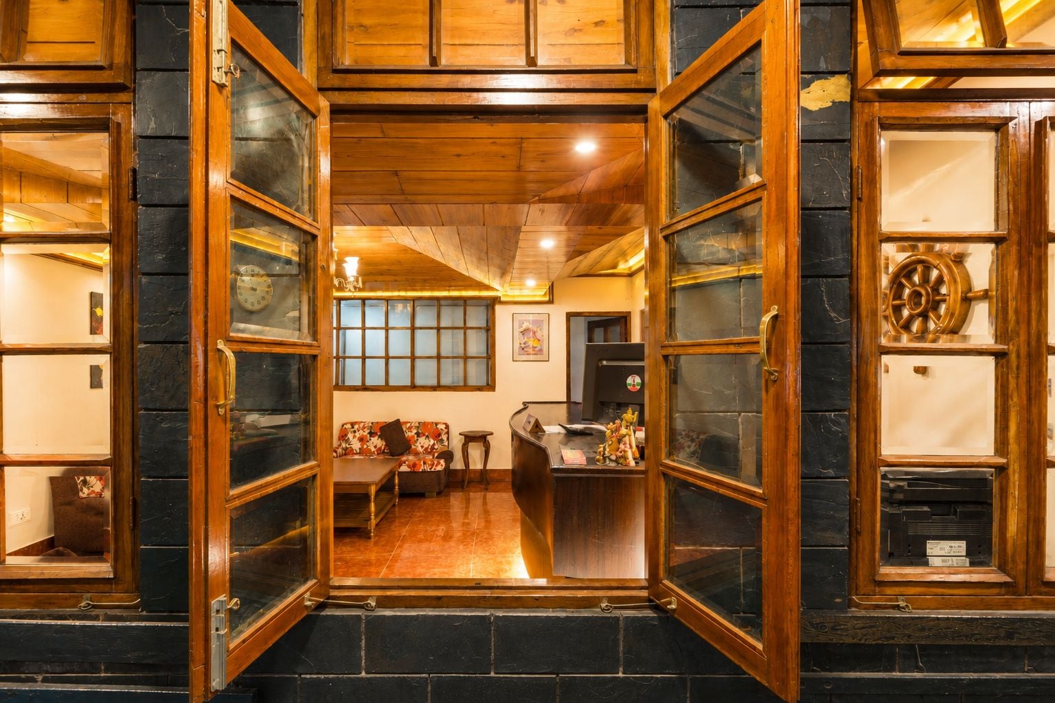 A hotel lobby with a wooden reception desk, a sofa, and a dining area.