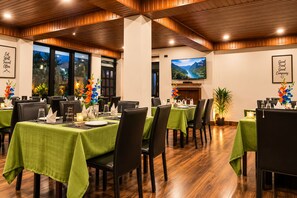 Un espace repas avec des tables dressées pour accueillir plusieurs convives, agrémenté de nappes vertes et de chaises noires.