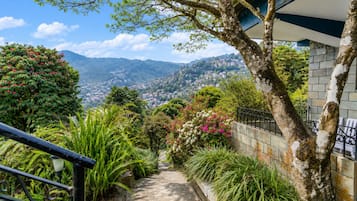 A staircase leading to a balcony overlooking a mountainous landscape with lush greenery and flowering plants.