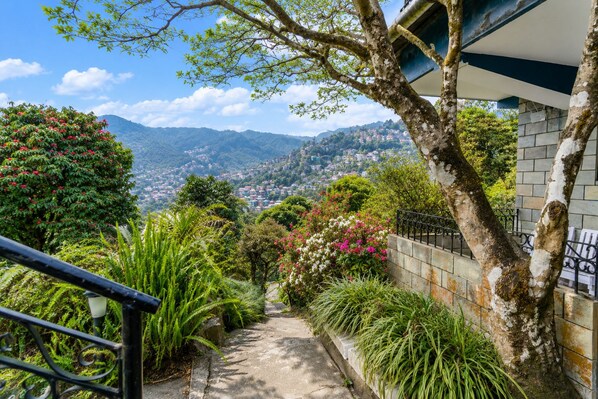 A staircase leading to a balcony overlooking a mountainous landscape with lush greenery and flowering plants.