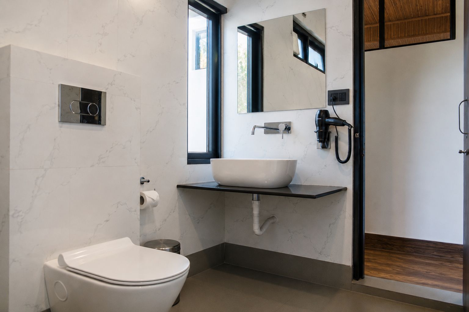 A modern bathroom with a white toilet, a vessel sink, a mirror, and a shower area.