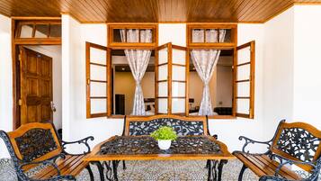 Quarto com teto de madeira, chão de azulejos, mesa com cadeiras e janela com cortinas.