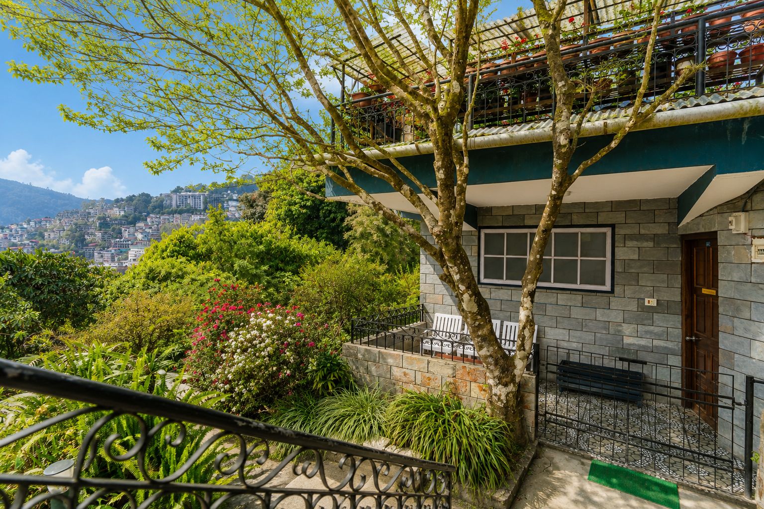 Un edificio residencial con balcón, rodeado de abundante vegetación y vistas a un paisaje urbano.
