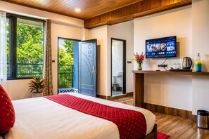 Une chambre d’hôtel avec un lit, une télévision, une petite étagère avec quelques objets et un balcon donnant sur un paysage verdoyant.
