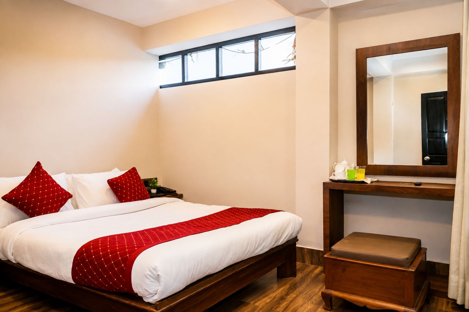 Quarto de hotel com cama, mesa de cabeceira, espelho, pequena mesa e um banco de madeira.