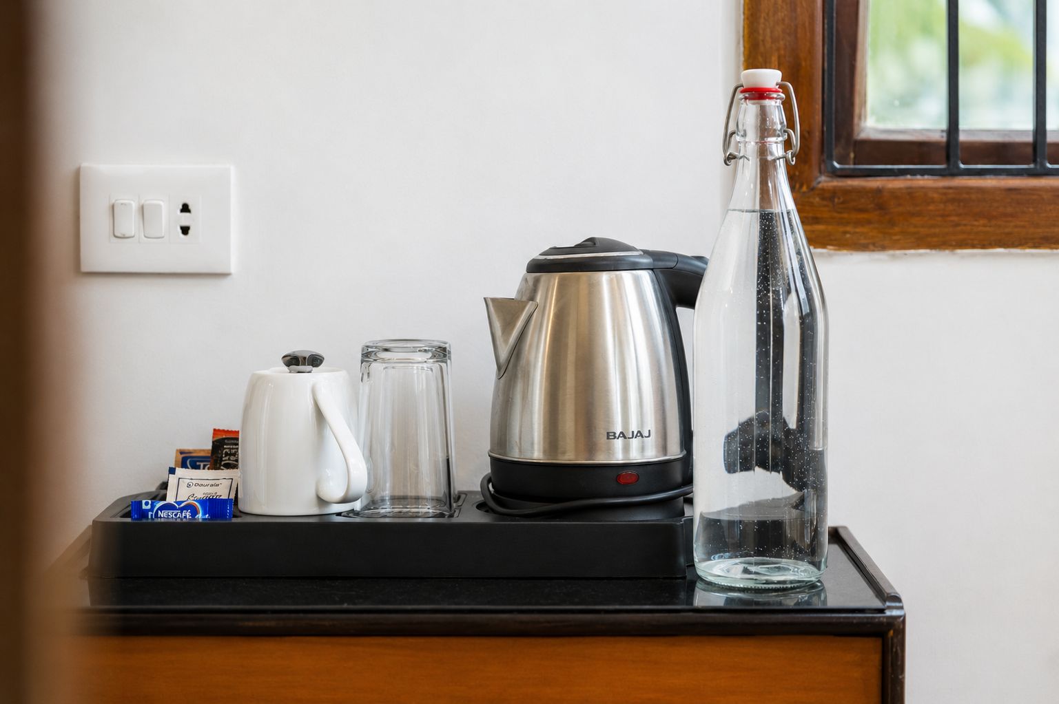 A kitchen counter with a coffee maker, a glass carafe, a kettle, and a bottle of water.