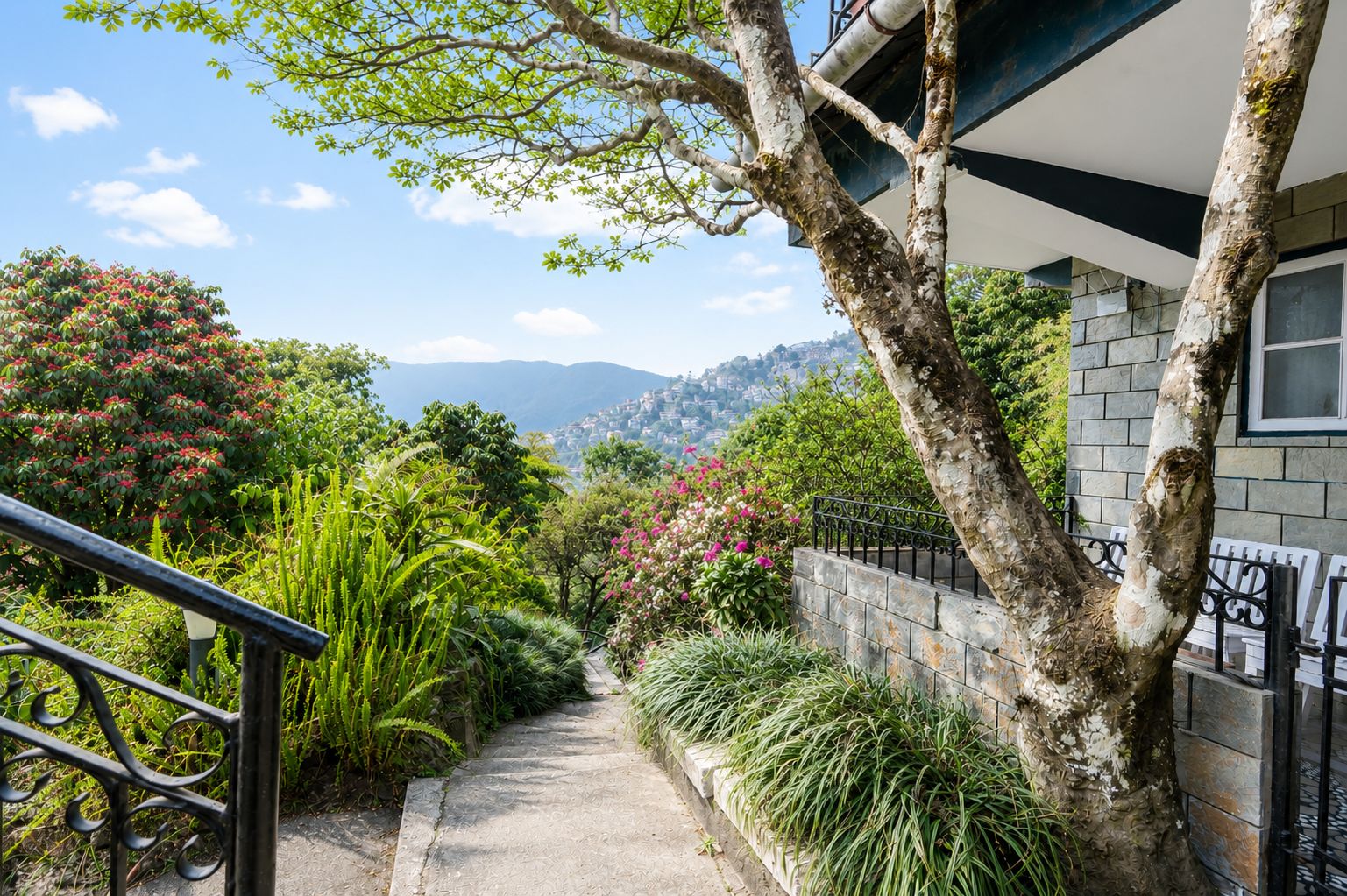 A pathway leading to a house with a stone wall and a metal railing on one side.