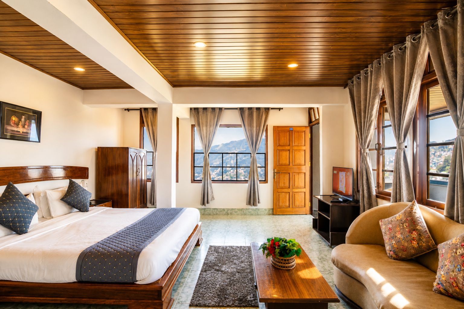 A hotel room with a bed, sofa, wooden ceiling, curtains, a television, and a window with a mountain view.