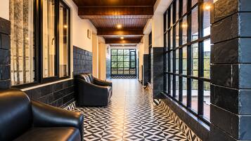 A hallway with black leather sofas, patterned floor tiles, and large windows with a view of greenery.