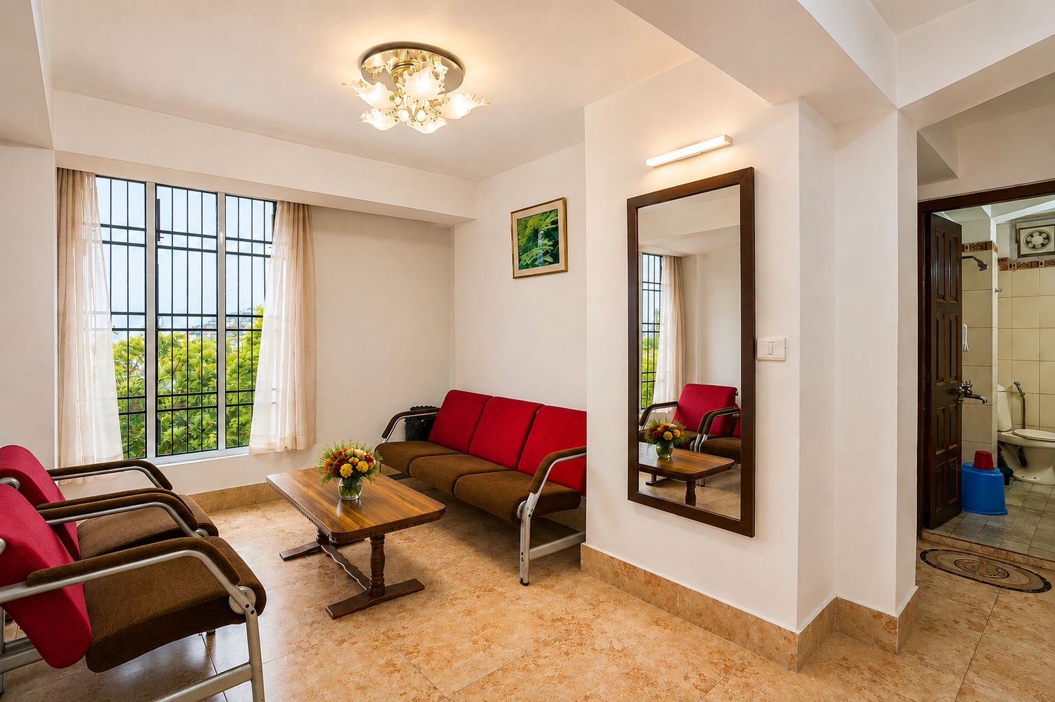 Ein Hotelzimmer mit Sofa, Sesseln, einem Couchtisch, einem großen Spiegel und einem Fenster mit Vorhängen.