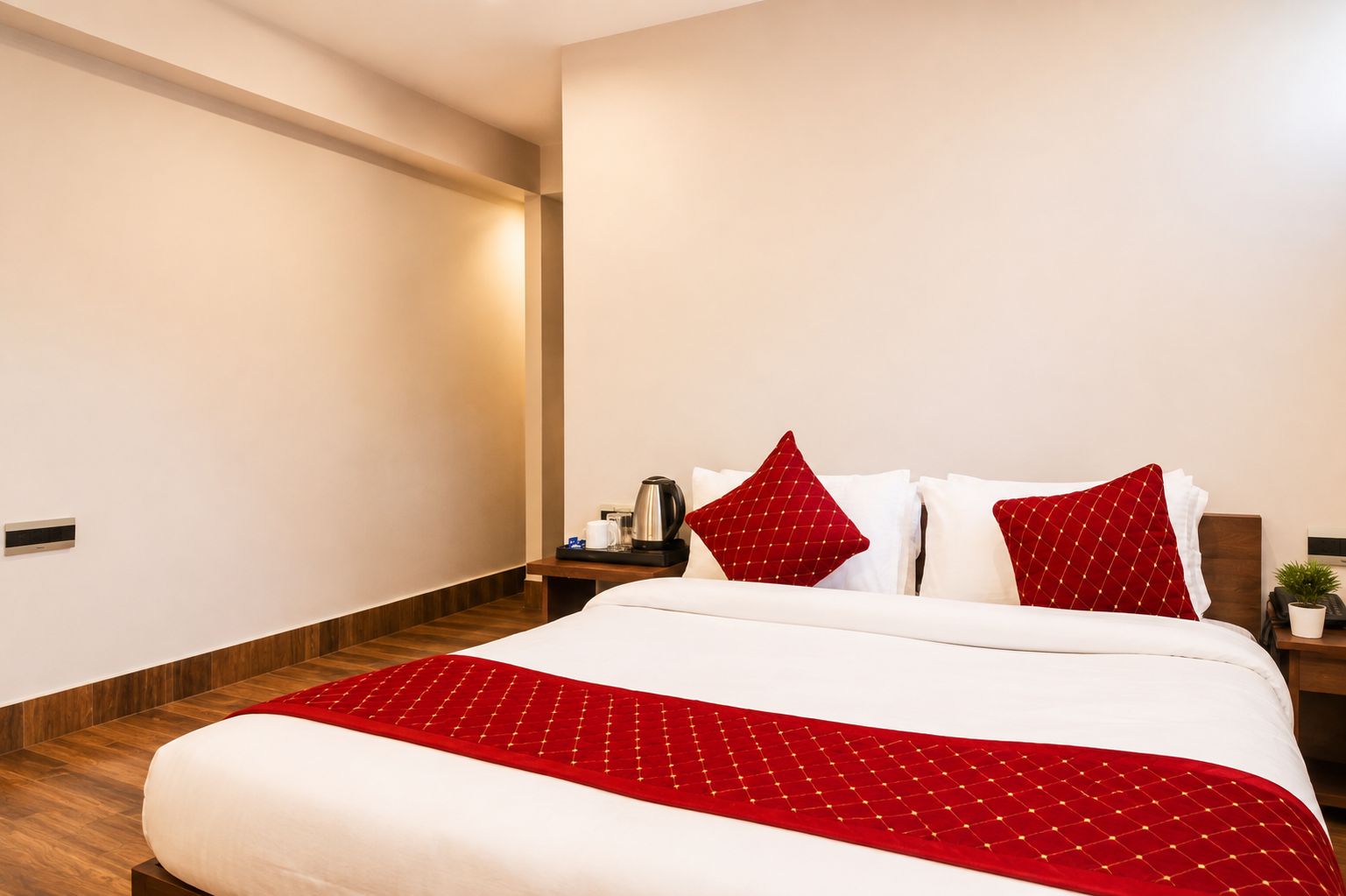 Une chambre d’hôtel avec un grand lit, un plancher en bois, une table de chevet avec une machine à café et une lampe fixée au mur.