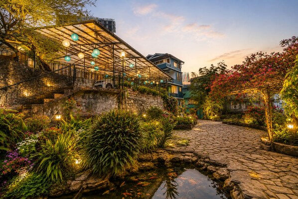 A garden pathway with a pond, stone steps, and a building with a balcony.