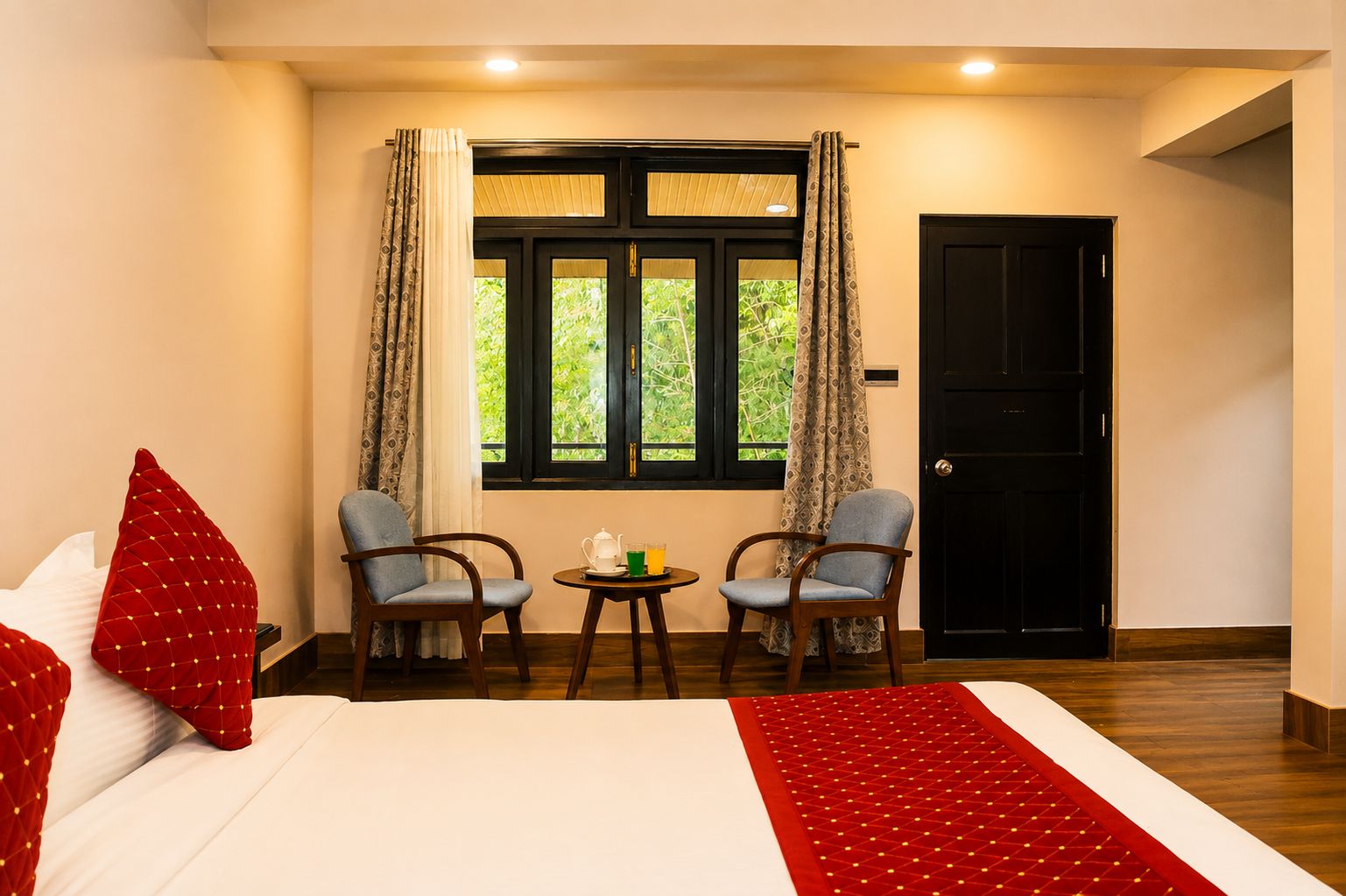 Une chambre d’hôtel avec un lit, deux fauteuils, une petite table avec une théière et des verres, et une fenêtre avec des rideaux.