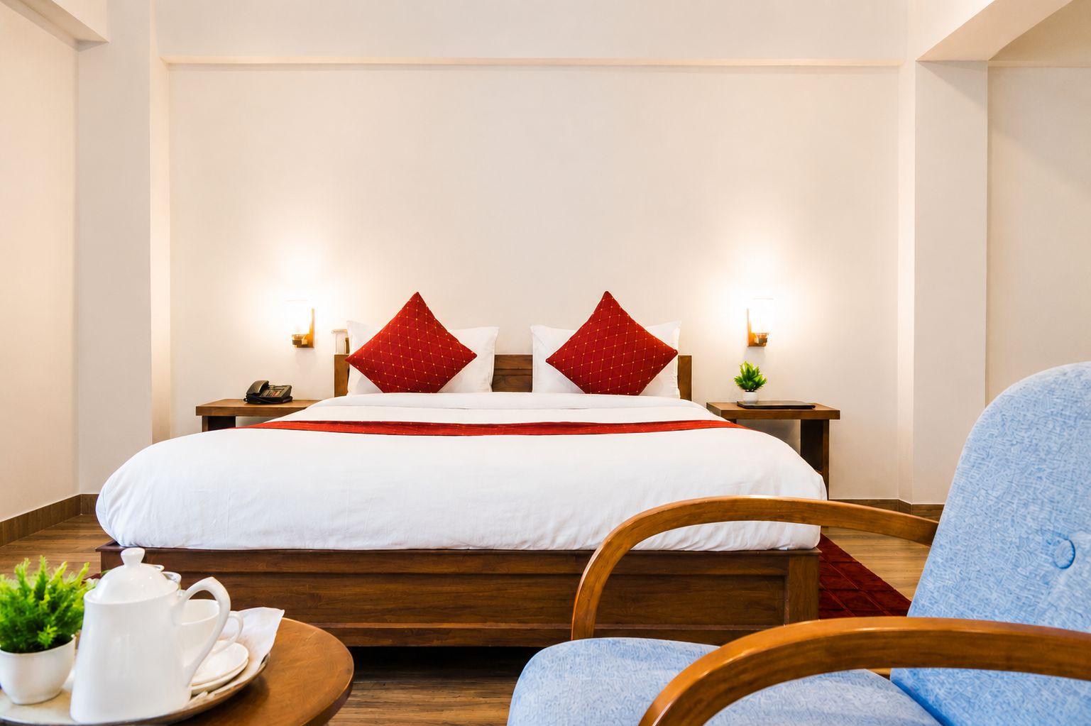 A hotel room with a bed, bedside tables, a coffee table with a teapot, and a chair.