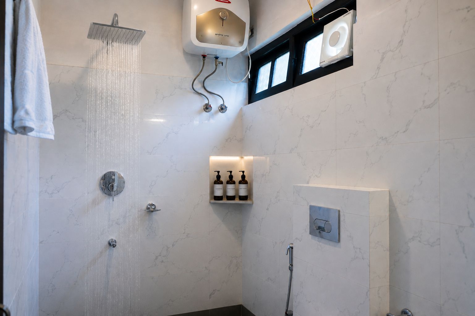 Un baño moderno con ducha, toallero, estante empotrado con artículos de aseo y una ventana.