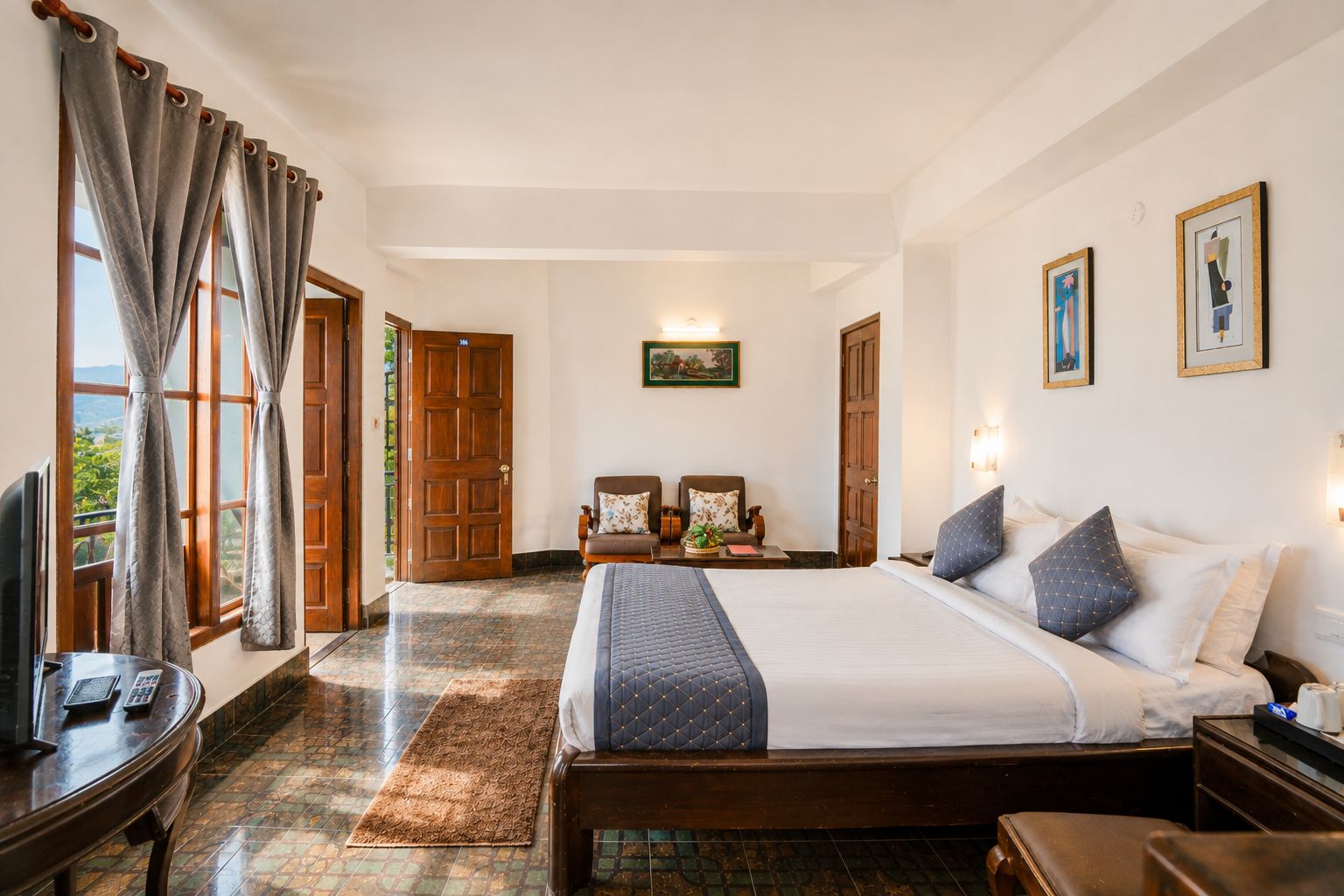 Habitación de hotel con una cama grande, un escritorio con teléfono, una silla y vistas al exterior a través de una puerta.