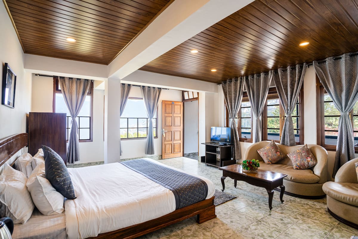 A spacious bedroom with a large bed, a sofa, a television, and a wooden ceiling.