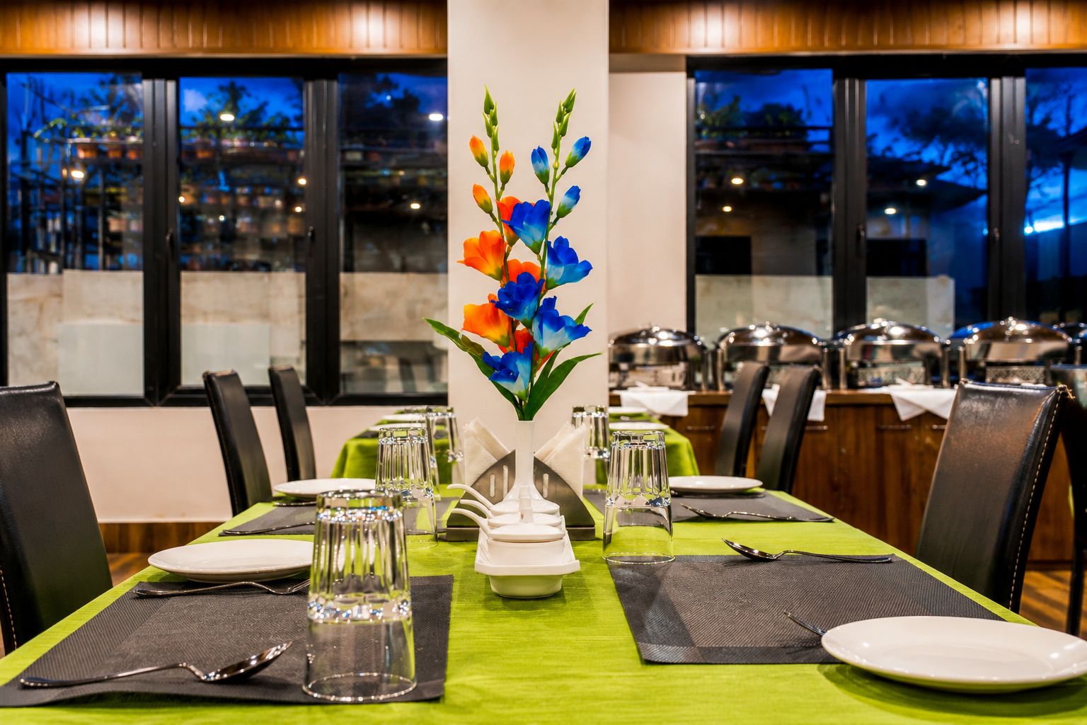 Een restaurant met een eethoek, een groene tafelkleed, witte borden en glazen.