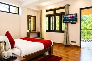 Une chambre d’hôtel avec un lit, une télévision, une fenêtre avec des rideaux et un balcon donnant sur un paysage verdoyant.