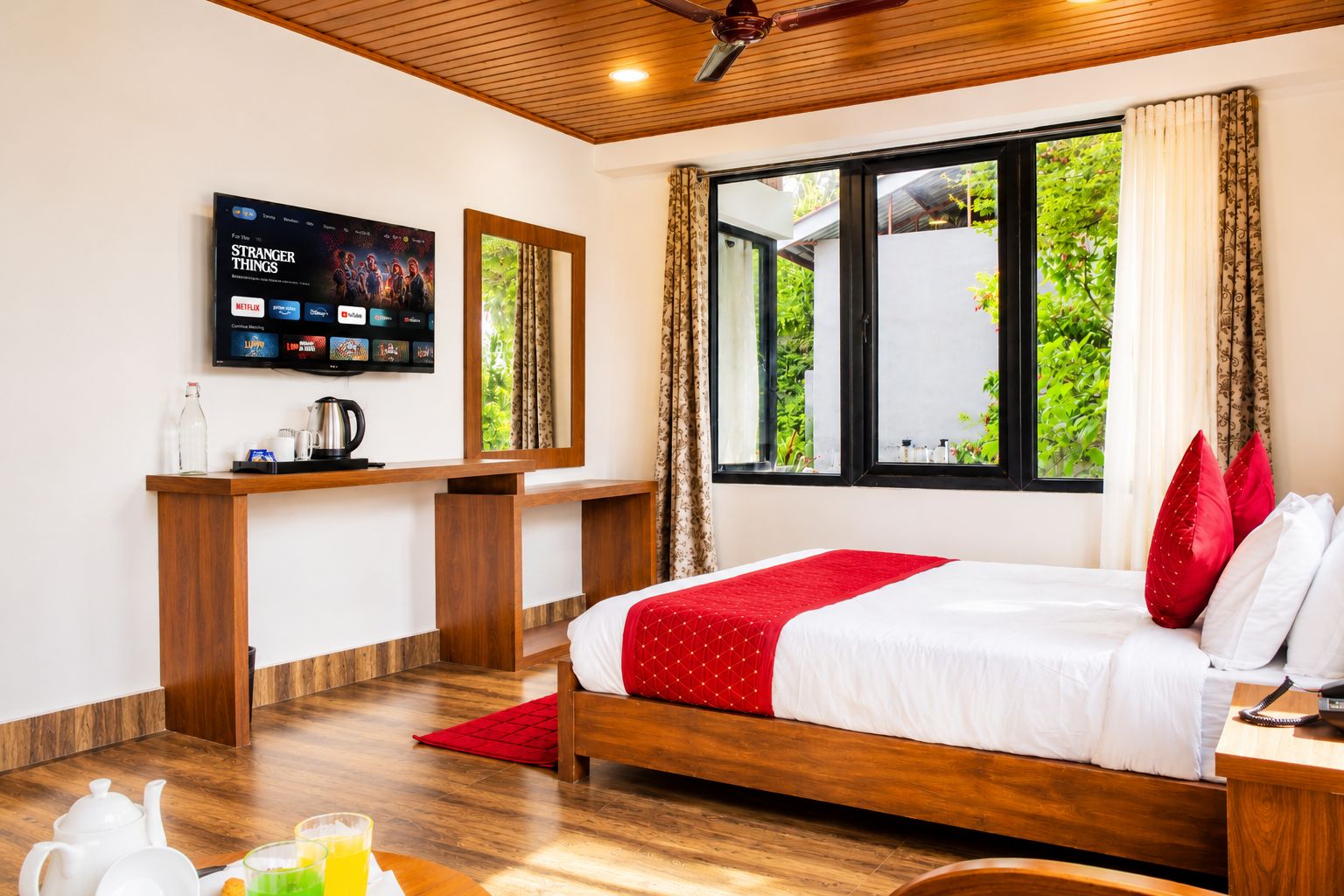 A hotel room with a bed, a desk, a television, and a window with a view of greenery.