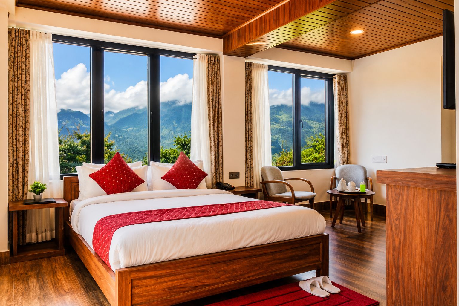 A hotel room with a large bed, two windows with mountain views, a desk, and a chair.
