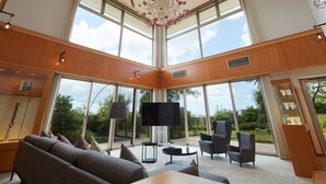 Un salón amplio con un televisor grande, asientos cómodos y ventanas grandes que ofrecen vistas al exterior.