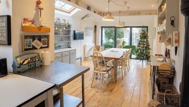 Una cucina con pavimento in legno, un tavolo da pranzo con sedie, un albero di Natale e vista sull'esterno.